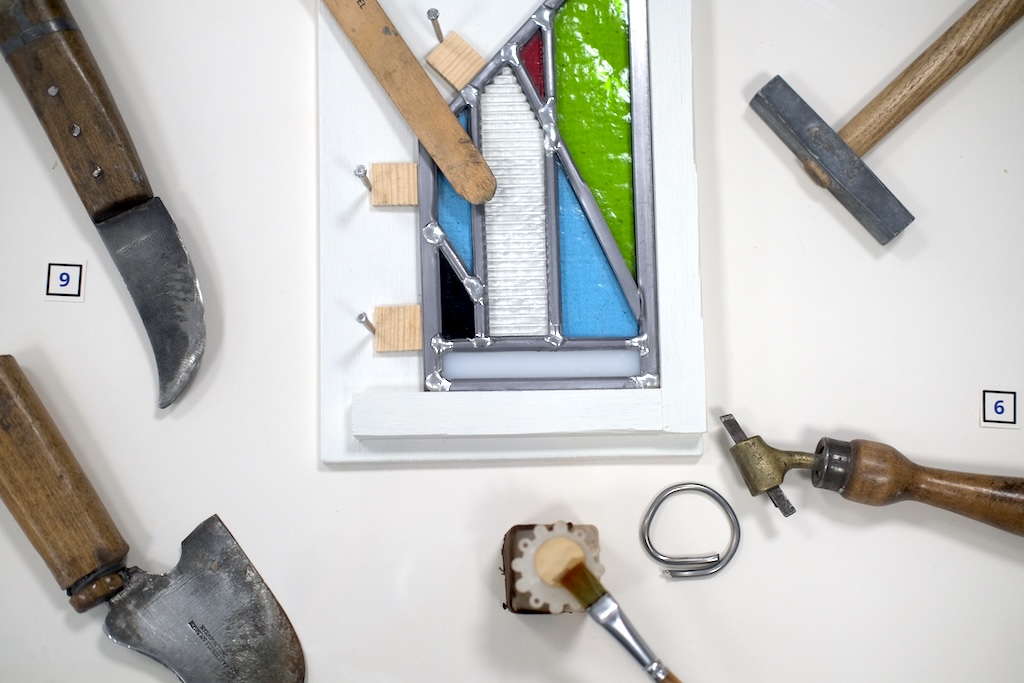 Close up of a stained glass sample surrounded by glass cutting tools, August, 2026 Photograph of stained glass sample and tools
